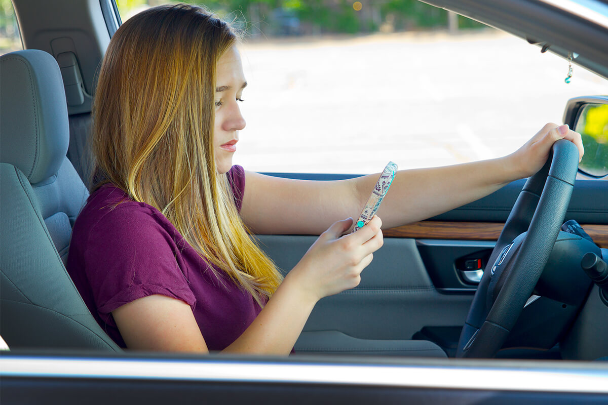 Teenage girl looking at a cell phone while in the driver's seat of a vehicle