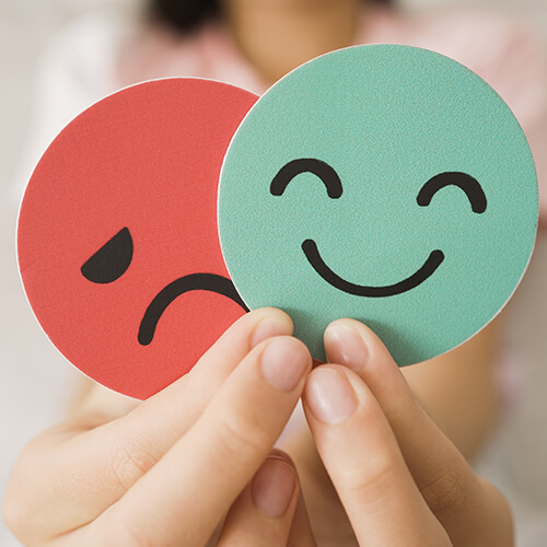 Hands holding sad face hiding behind happy face