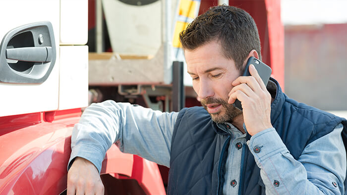 Man leaning against the cab of a semi-truck while talking on the phone