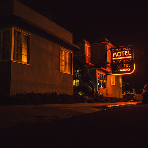 View of a lit motel sign from a street a night, with vehicles parked