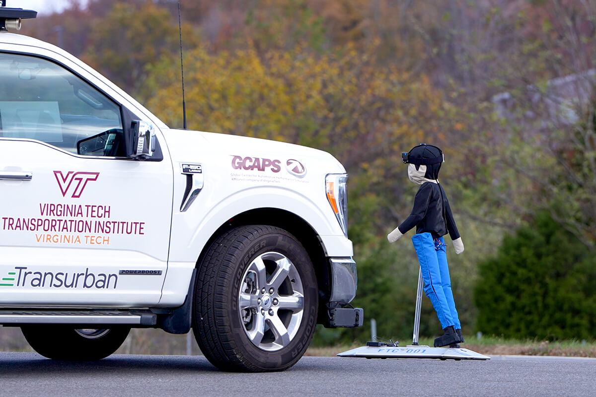 A VTTI vehicle faces a pedestrian test dummy on a road during a safety research setup.