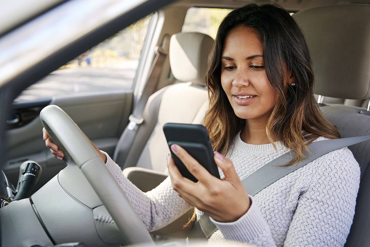 Woman looking at cell phone while in the driver's seat of a car
