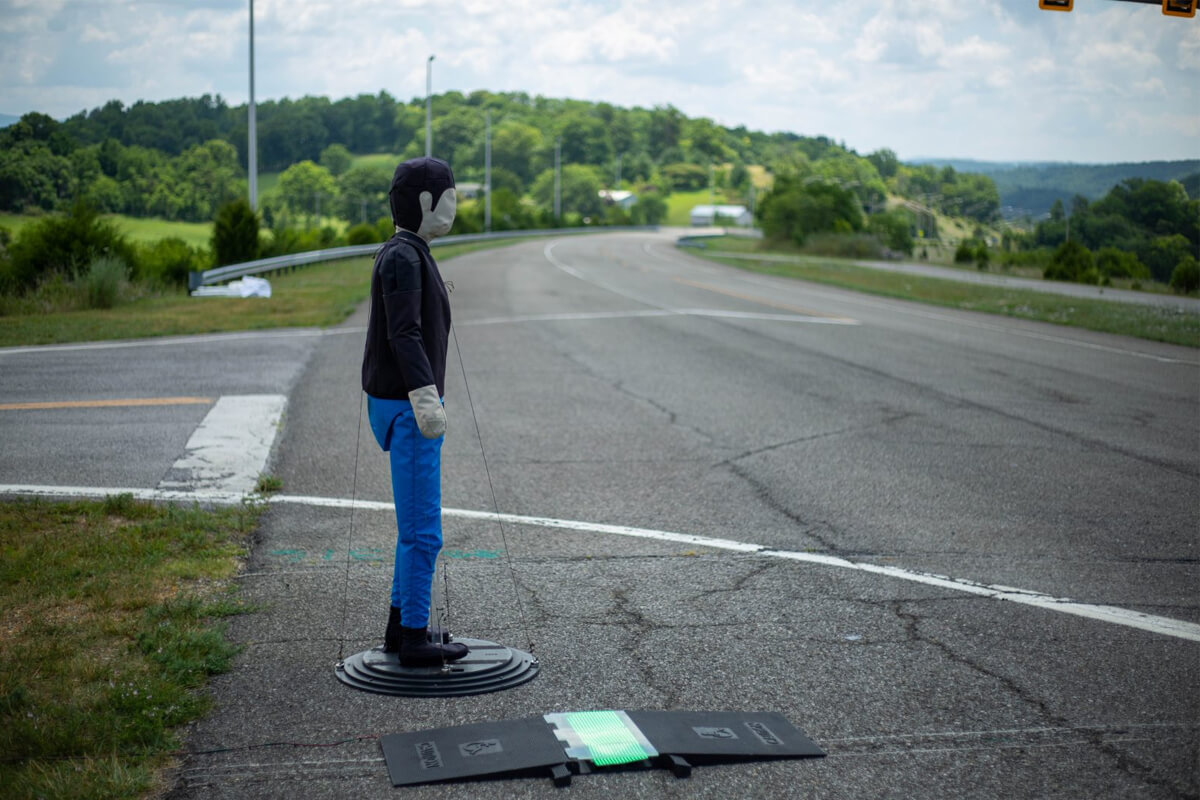 A robotic pedestrian stands next to an LED pedestrian alert footboard.